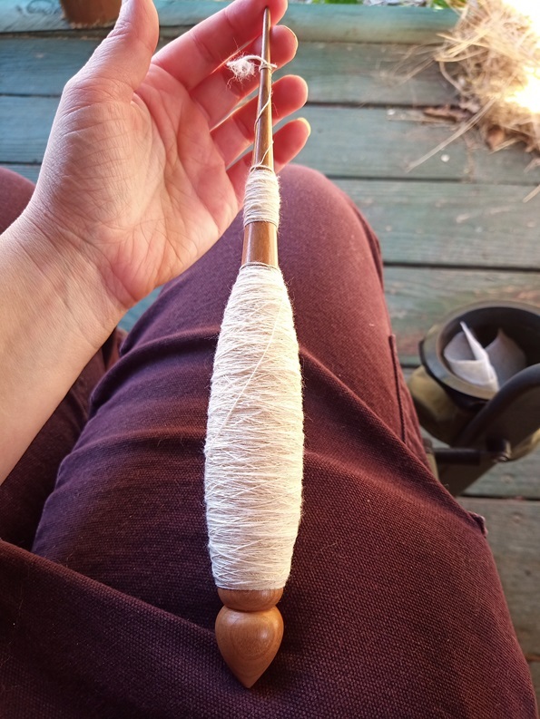 A brown wooden spindle loaded with white cotton singles. 