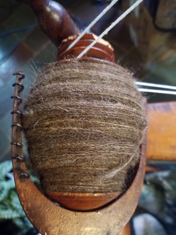 A marled brown yarn on a wooden wheel bobbin.