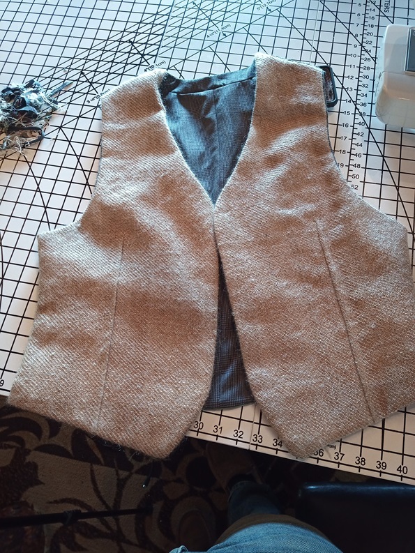 A tan colored waistcoat with grey lining is laying on a measuring table.