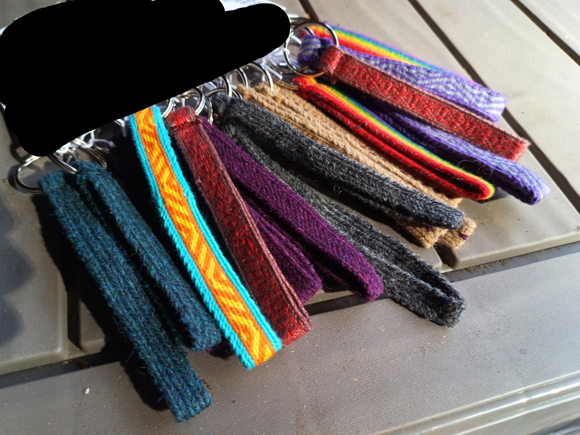 A pile of key fobs in various colors of tablet woven bands.The corner of the picture is blacked out to hide something