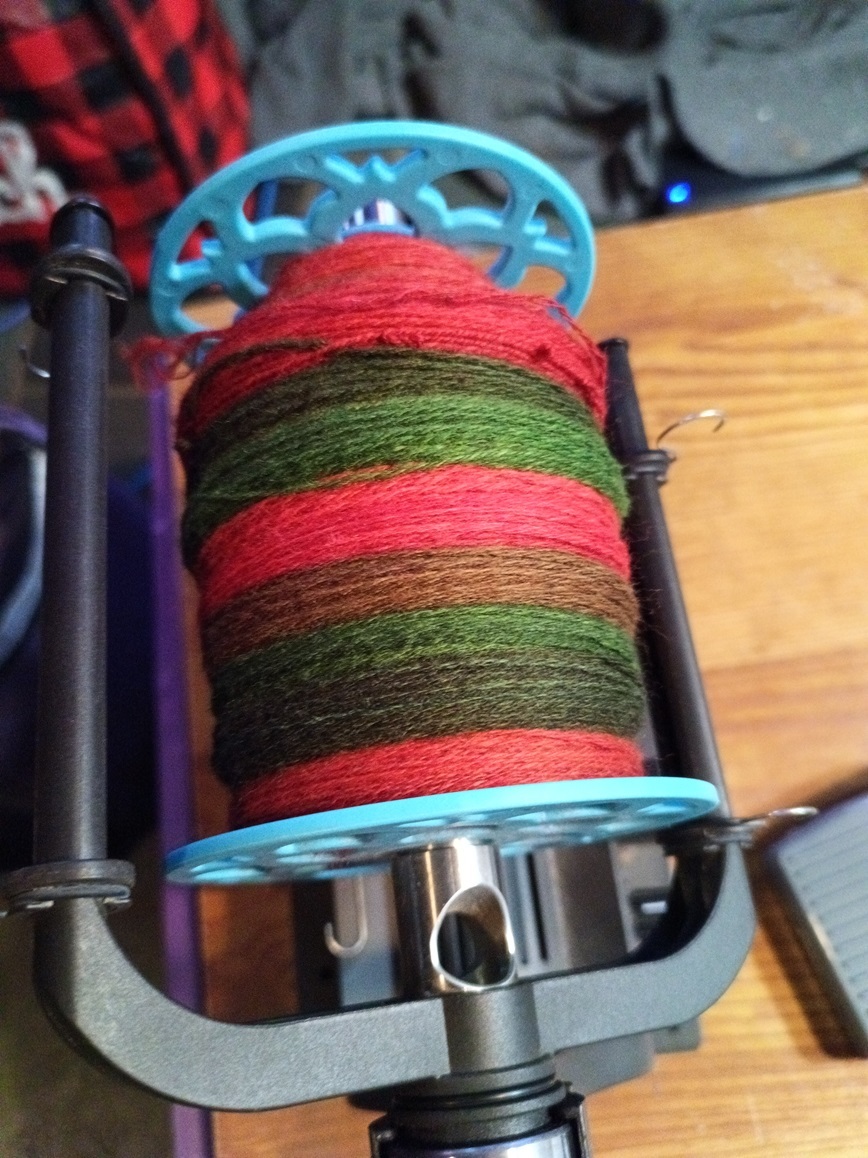 A bobbin half filled with fine yarn in red and green.