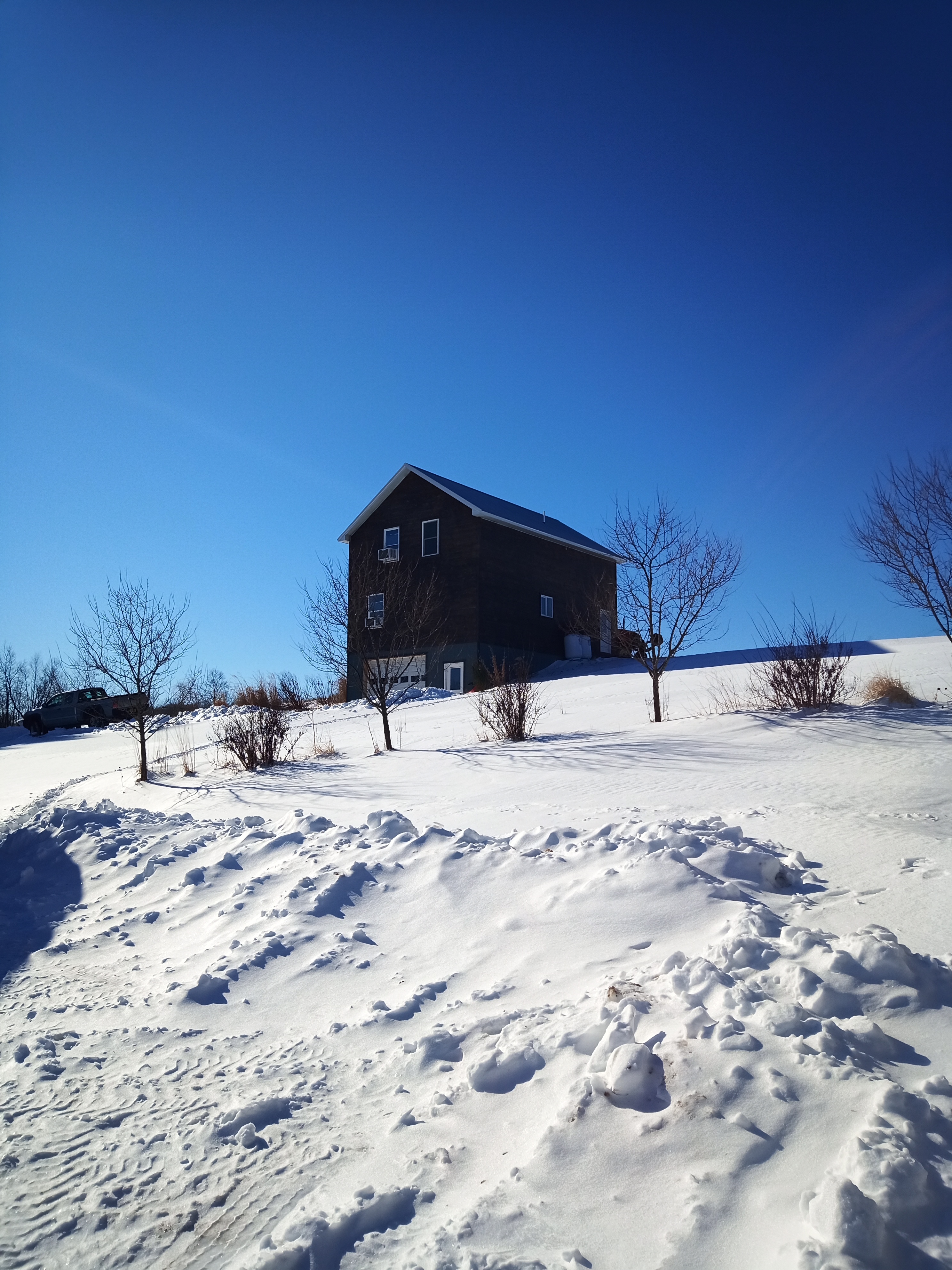 A three story barn is at the top of a steep snow covered hill.