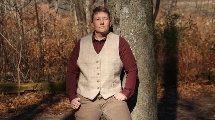 A person leaning against the tree wearing a red buttonup shirt and the tan waistcoat.