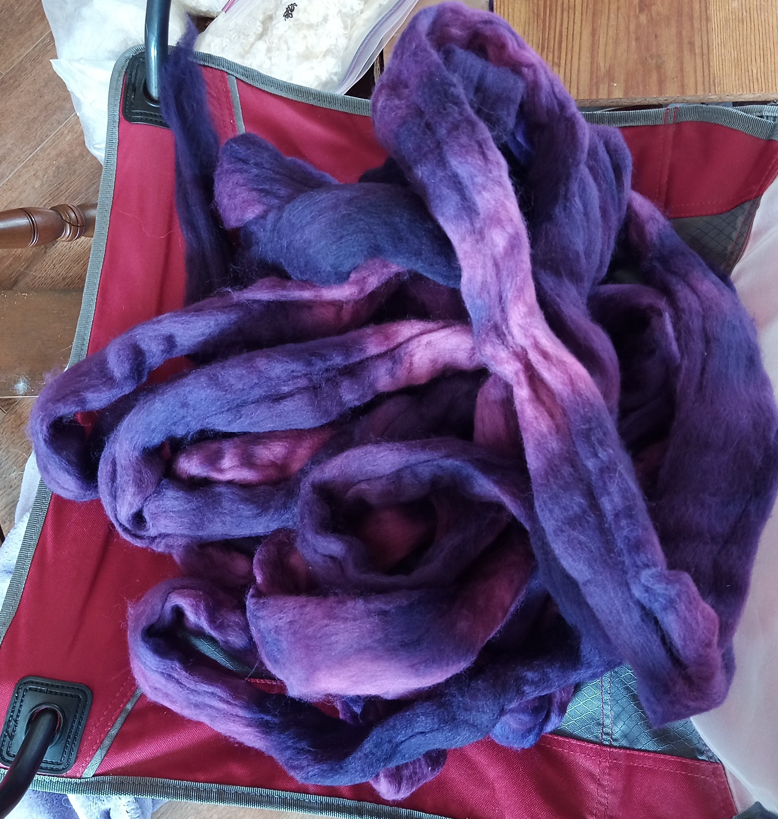 A pile of purple roving sitting on a red camp chair. The roving is mostly a deep purple with lavender sections.