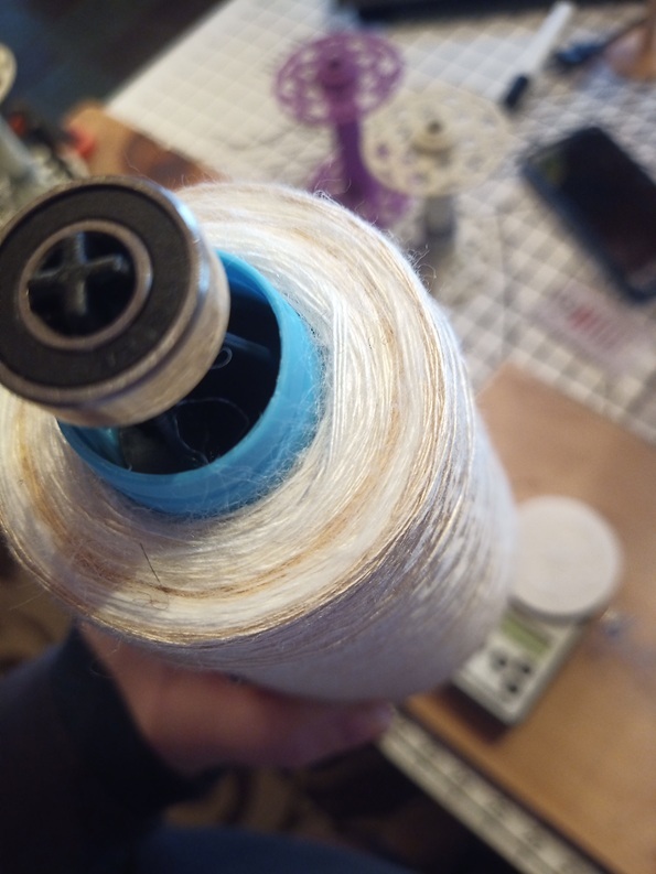 The bottom side of a small cone of yarn, showing the different shades of the plant fibers, some are creamy, some are bright white and one is tan.
