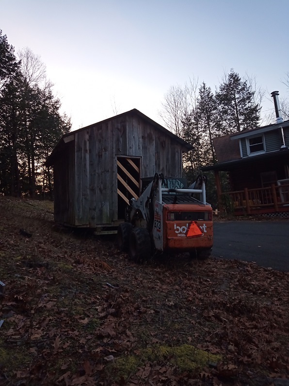 A bobcat pulling the shed, there are bracers across the doorway infront of the bobcat.