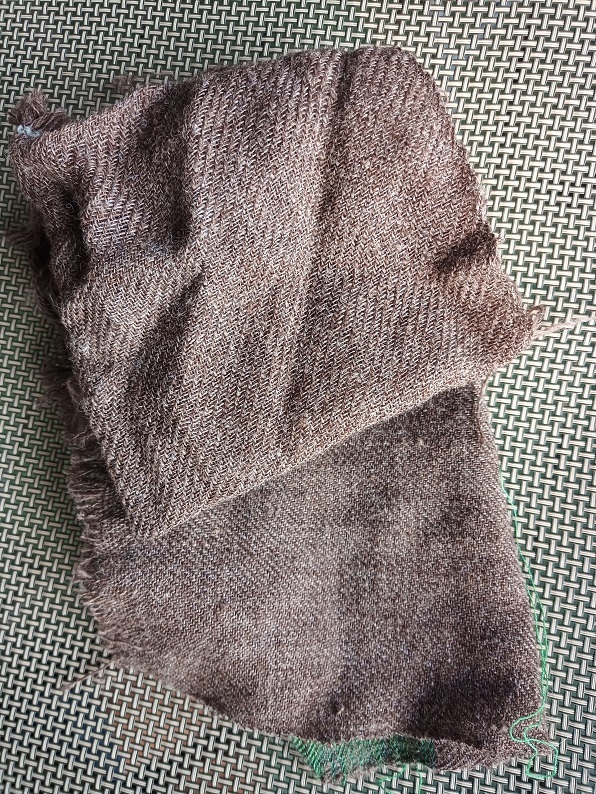 Two pieces of brown twill cloth are sitting on a woven grey background.