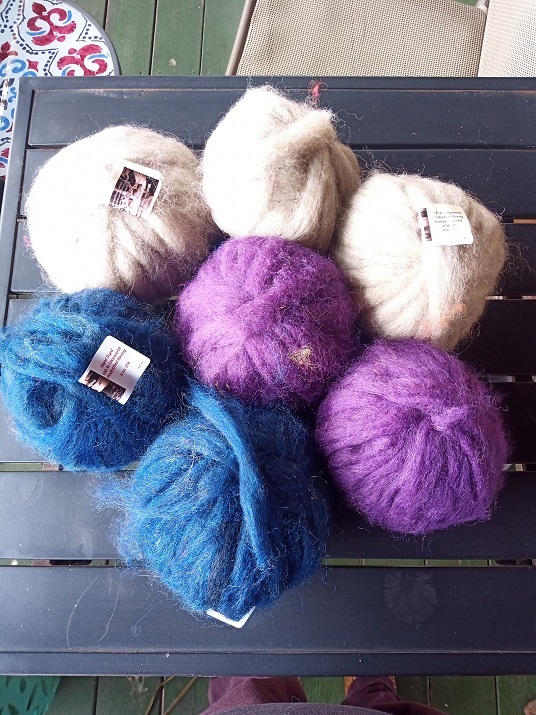 Seven balls of fluffy soft roving are sitting on a table. They look squishy.