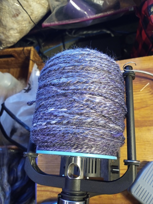 A super squishy squashy bobbin of yarn. It is a dark, shimmery purple black color.