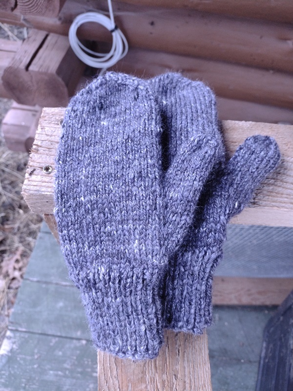 A deep purple pair of mittens are sitting on a chunk of wood.