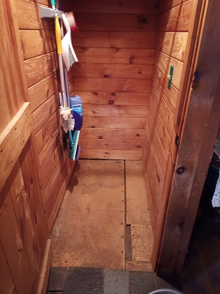 A wooden sided closet with a shitty plywood floor.