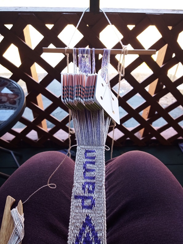 A tablet woven band with a little fire like symbol at the bottom and the word "damn" woven.
